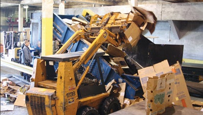 Star Photo/Abby Morris-Frye Workers at the Carter County Recycling Center use a piece of heavy equipment to drop cardboard onto a conveyor belt. The cardboard then moves up the belt into the compactor where it is then baled.