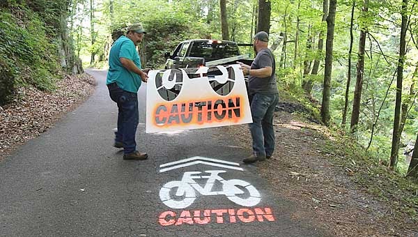 Star Photo/Abby Morris-Frye  Carter County Parks and Recreation Committee member Mel McKay, left, and Carter County Highway Committee Chairman Mike Hill remove a stencil from the road after a caution symbol was painted on Old Railroad Grade Road to advise motorists that bicyclists may be using the roadway. The markings are part of the county's preparation for extending the Tweetsie Trail to Roan Mountain.
